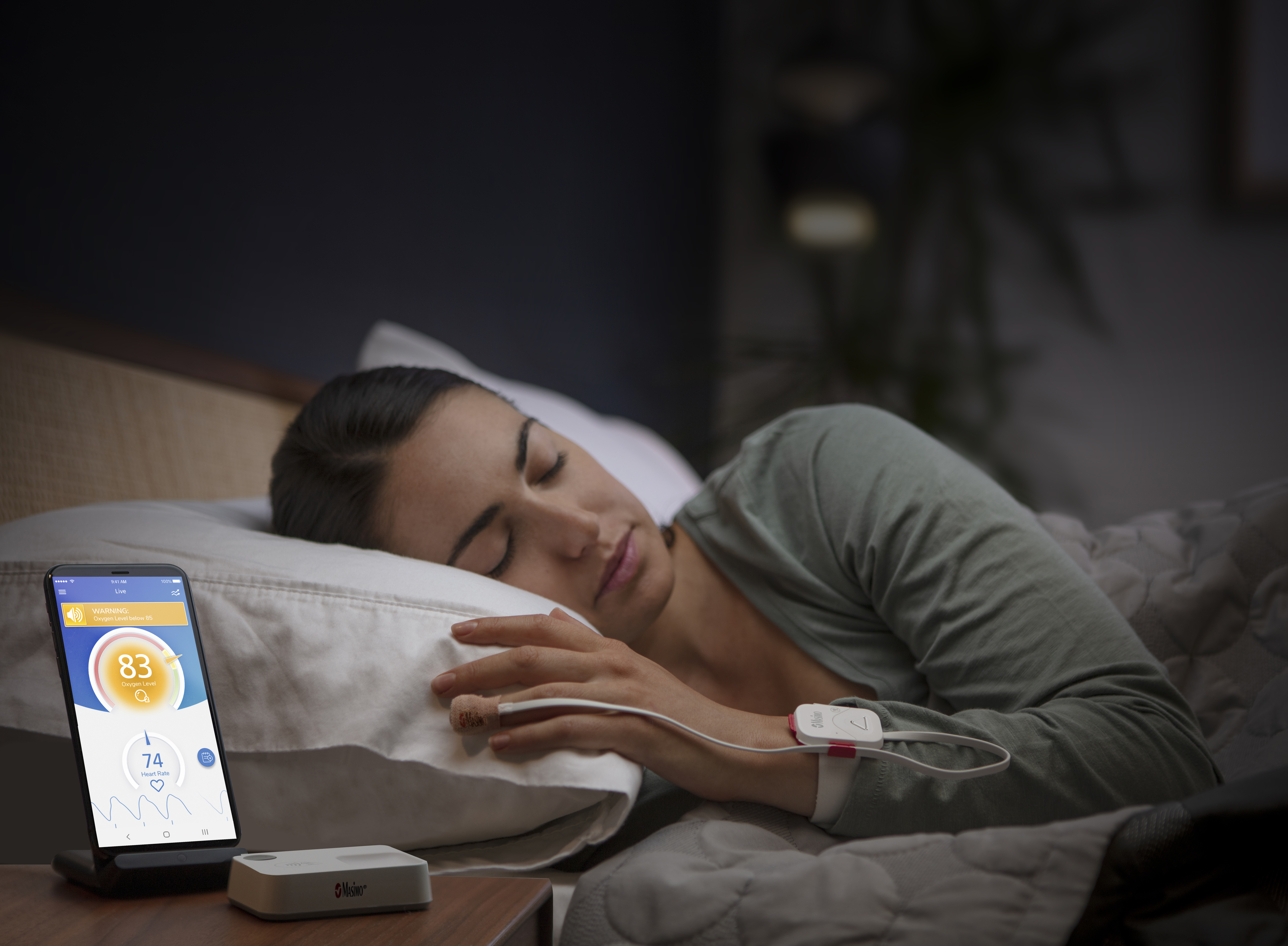 Woman in bed wearing Safetynet Alert next to phone displaying Safetynet App Screen
